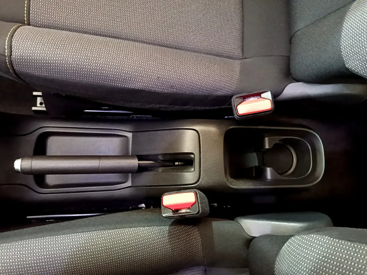 Vue plongeante sur la console centrale noire entre les sièges avant gris foncé de la Citroën C3 blanche.