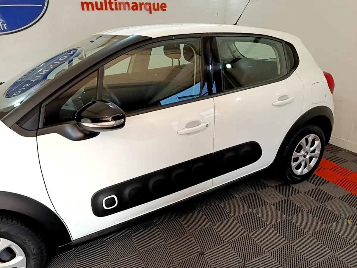 Profil côté gauche d'une Citroën C3 blanche avec protections noires caractéristiques sur les portières.
