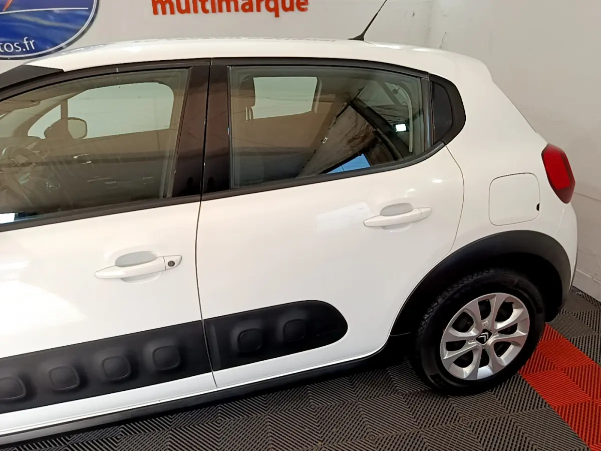 Profil côté gauche d'une Citroën C3 blanche avec protections latérales noires et jantes alliage visibles.