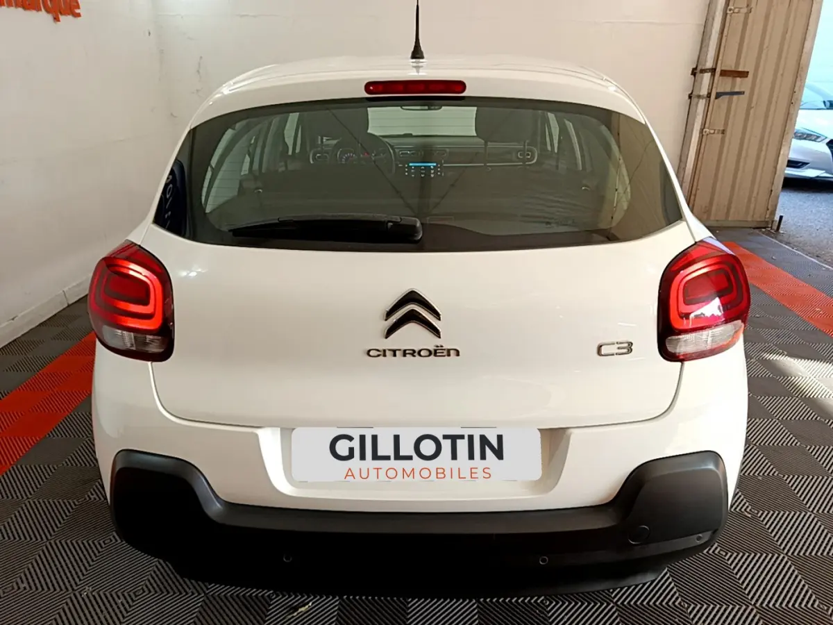 Vue arrière d'une Citroën C3 blanche 2019 avec feux arrière allumés et logo centré sur un sol à damiers.