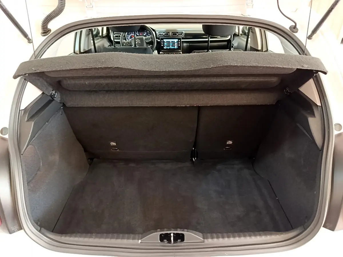 Coffre ouvert d'une Citroën C3 blanche 2019, vue intérieure vers l'avant avec tableau de bord et écran tactile visibles.