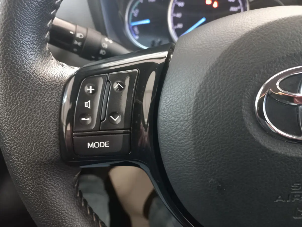 Gros plan sur les commandes gauche du volant en cuir noir de la Toyota Yaris 1.5 VVT-I HYBRID 2018.