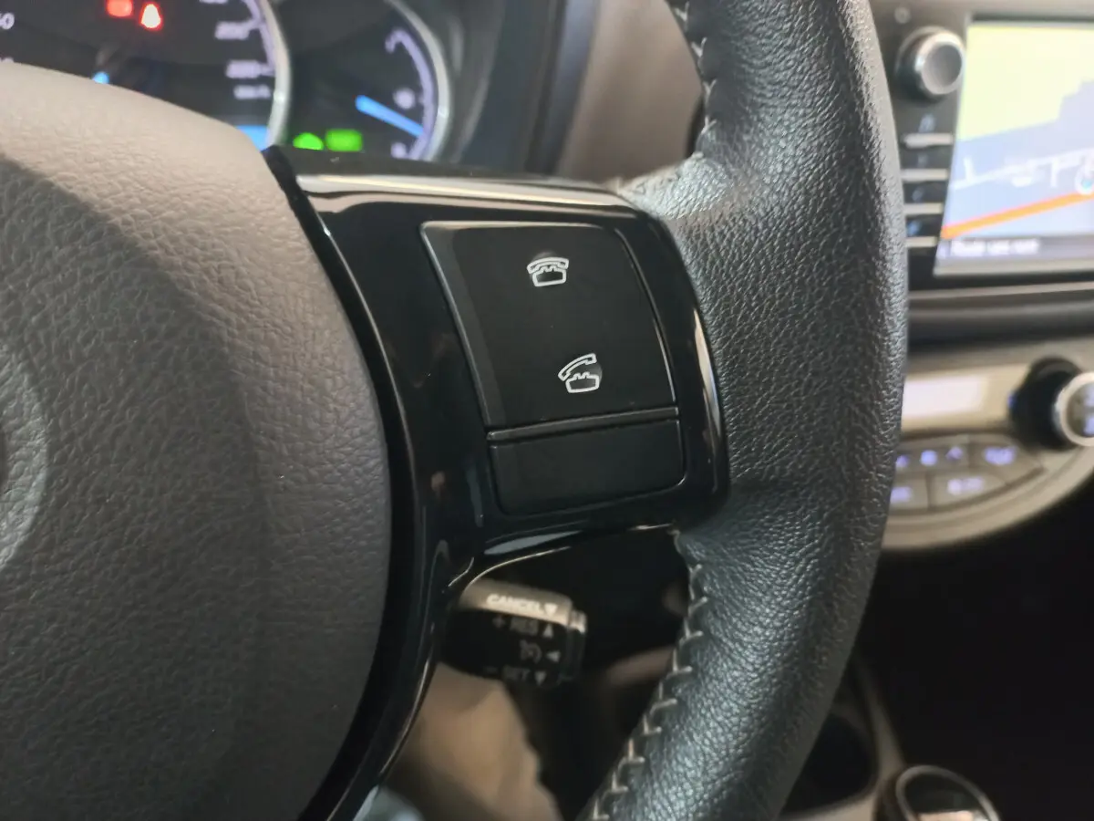 Gros plan sur les commandes téléphoniques du volant cuir noir de la Toyota Yaris hybride 2018 avec écran tactile en arrière-plan.