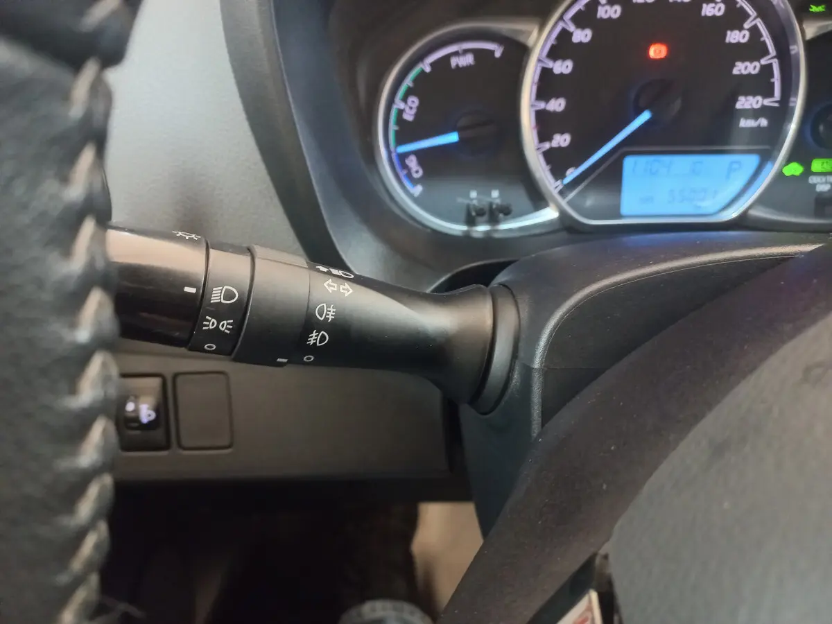 Gros plan sur la manette des phares à gauche du volant d'une Toyota Yaris hybride 2018, tableau de bord éclairé.