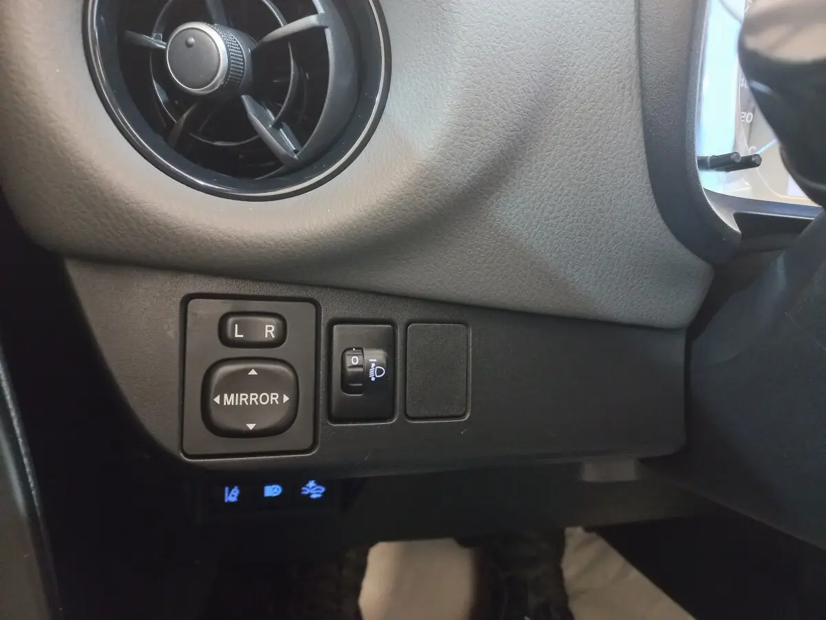 Détail des commandes de réglage des rétroviseurs et phares côté gauche dans l'habitacle de la Toyota Yaris noire 2018.