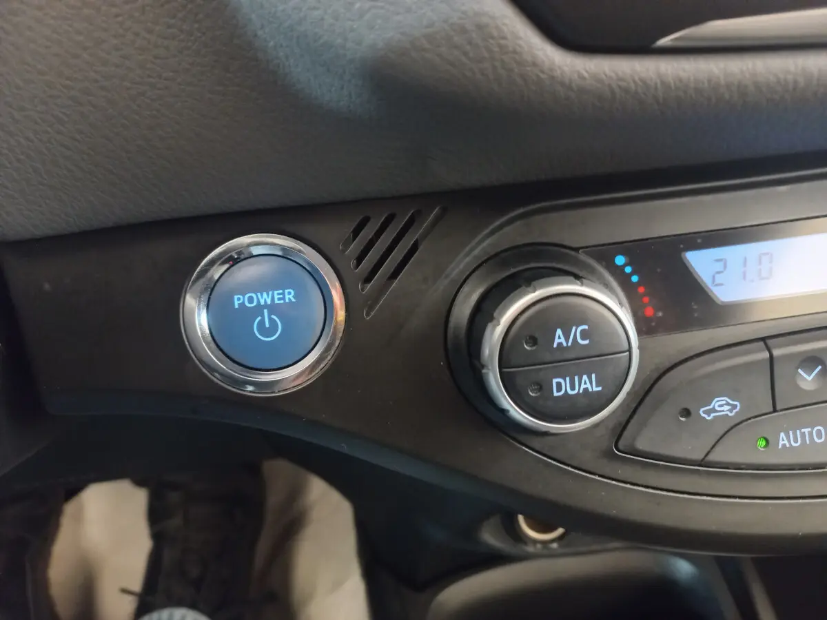 Détail du tableau de bord noir de la Toyota Yaris hybride 2018 avec bouton démarrage bleu et commandes climatisation digitale.