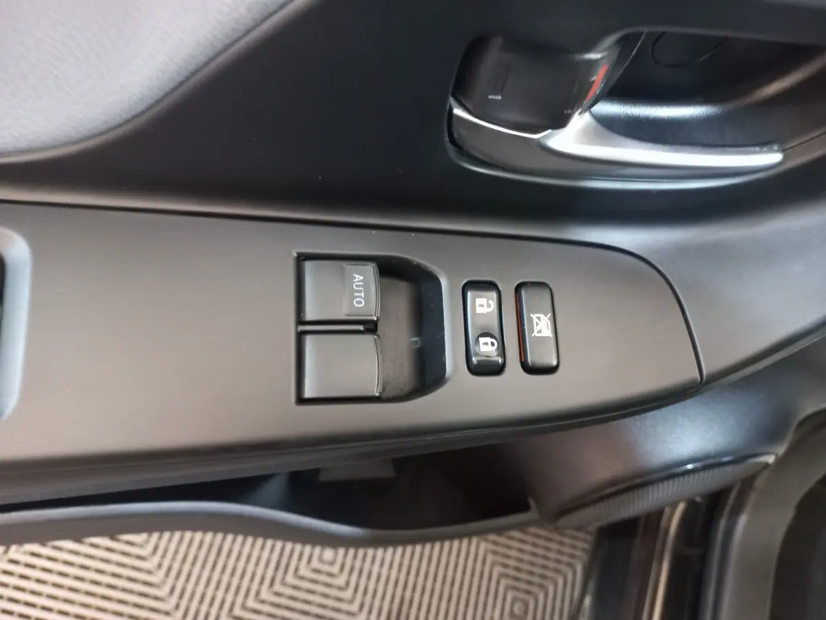 Gros plan sur la commande des vitres et verrouillage côté conducteur de la Toyota Yaris noire 2018, intérieur sobre.