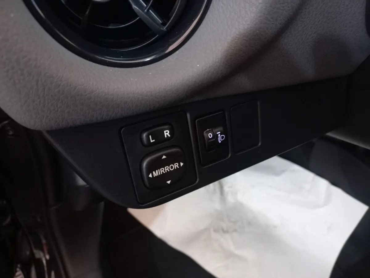 Gros plan sur les commandes de réglage des rétroviseurs et des phares d'une Toyota Yaris noire, côté conducteur.