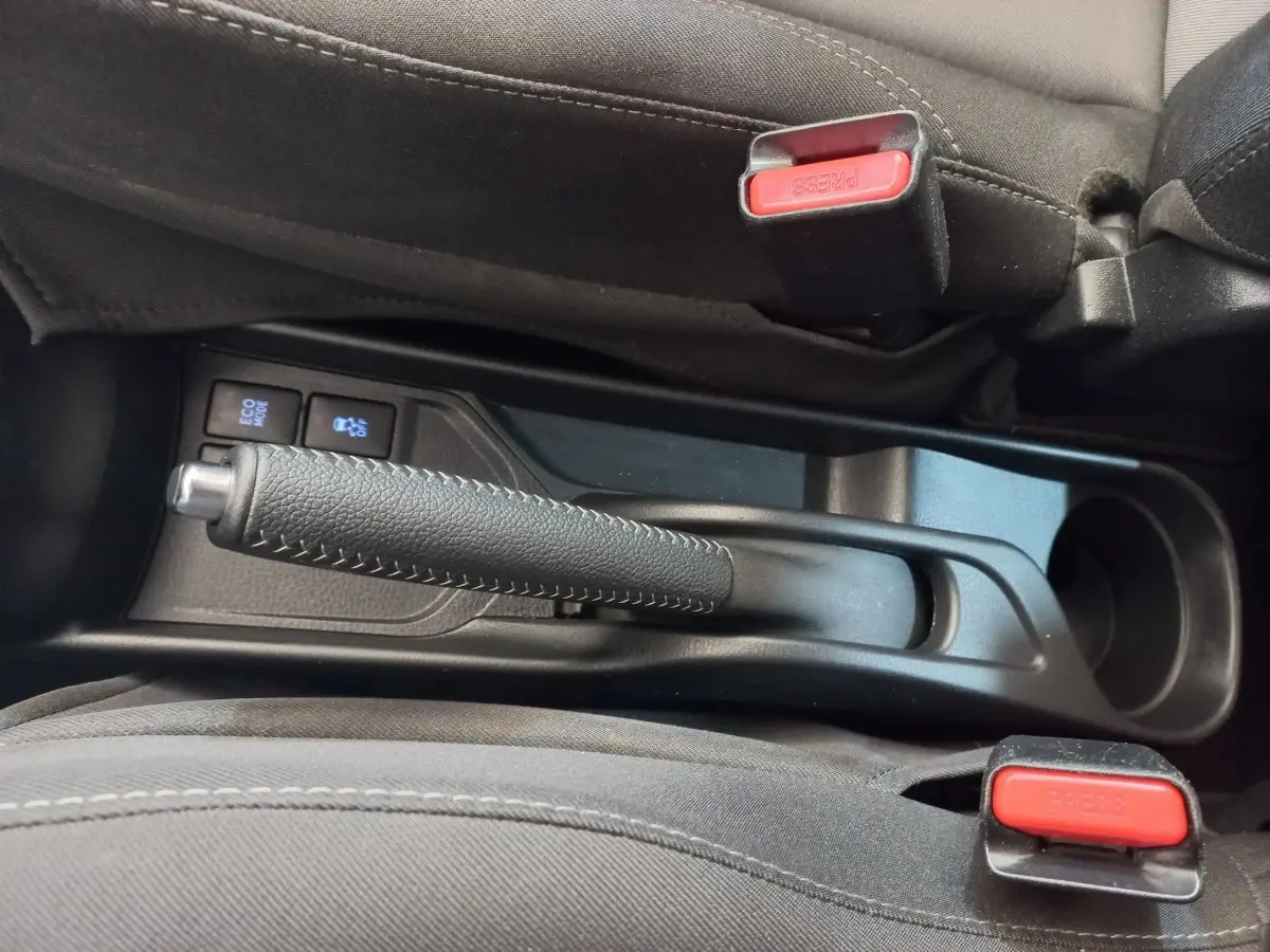 Vue rapprochée de la console centrale noire de la Toyota Yaris 2018, montrant frein à main et boutons Eco Mode et traction.