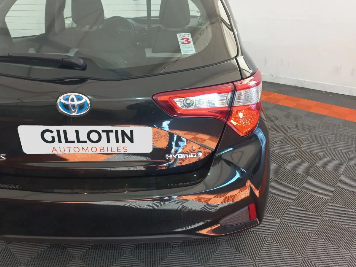 Vue arrière droite d'une Toyota Yaris hybride noire avec feux arrière distinctifs et logo Hybrid visible.