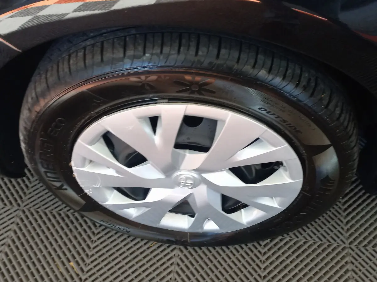 Gros plan sur la roue avant droite d'une Toyota Yaris noire, avec enjoliveur argenté et pneu Hankook.