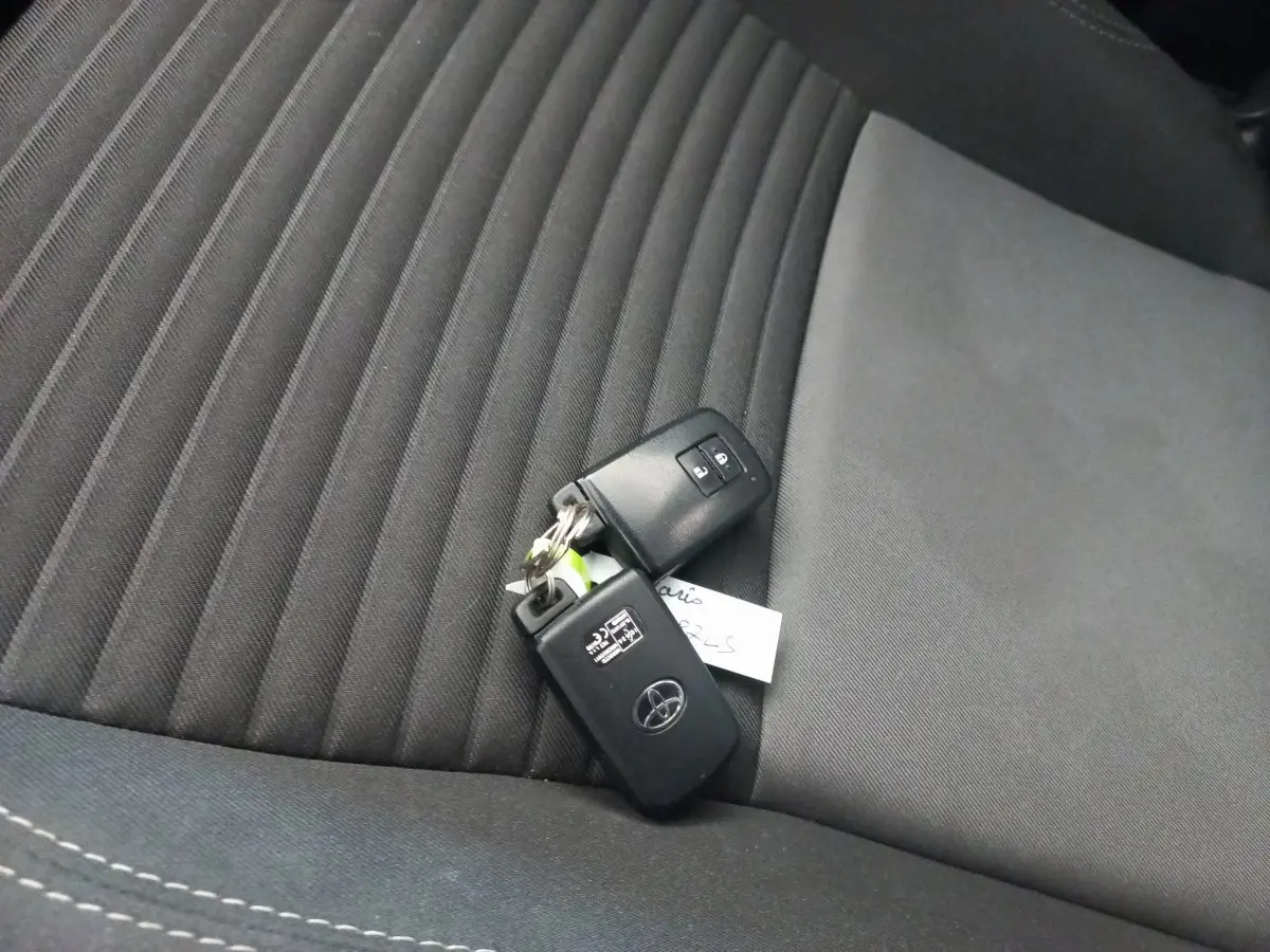 Clé de voiture Toyota posée sur un siège avant en tissu noir à motifs rayés, intérieur sobre et moderne.