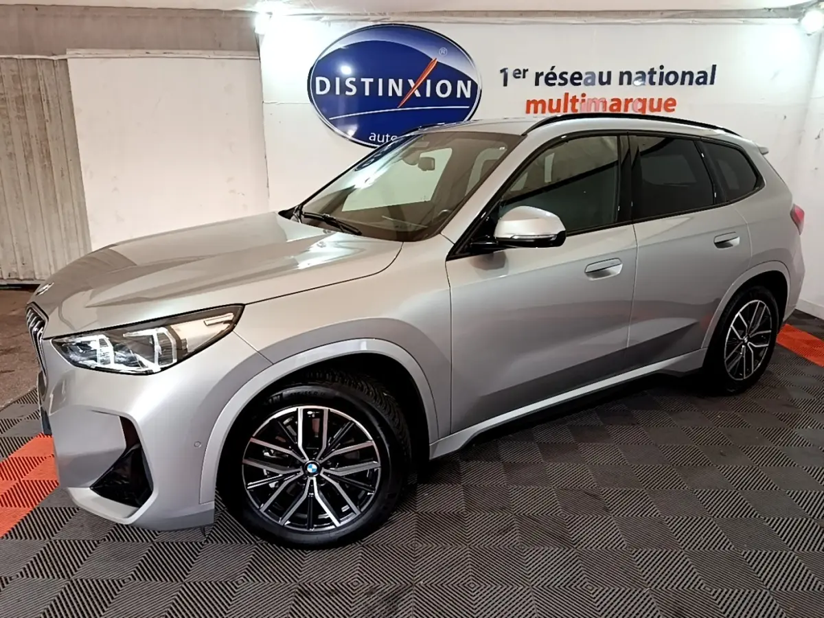 BMW X1 xDrive23i M Sport gris clair vue de profil droit en intérieur avec jantes noires et toit noir.