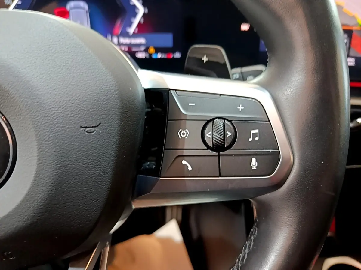 Gros plan sur les commandes du volant cuir noir du BMW X1 xDrive23i M Sport 2023, boutons multifonctions visibles.