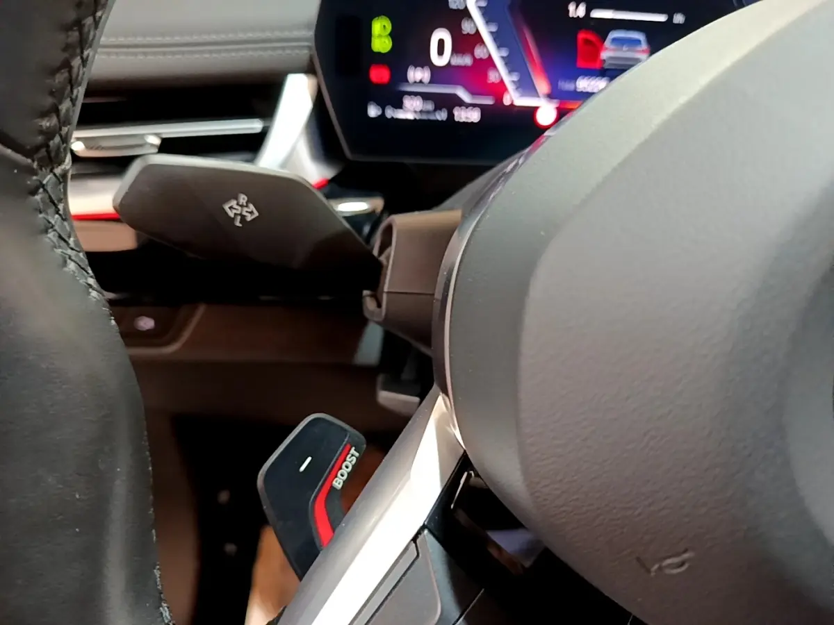 Gros plan sur le volant cuir et alu d’une BMW X1 xDrive23i M Sport 2023, avec palette Boost et tableau de bord numérique.