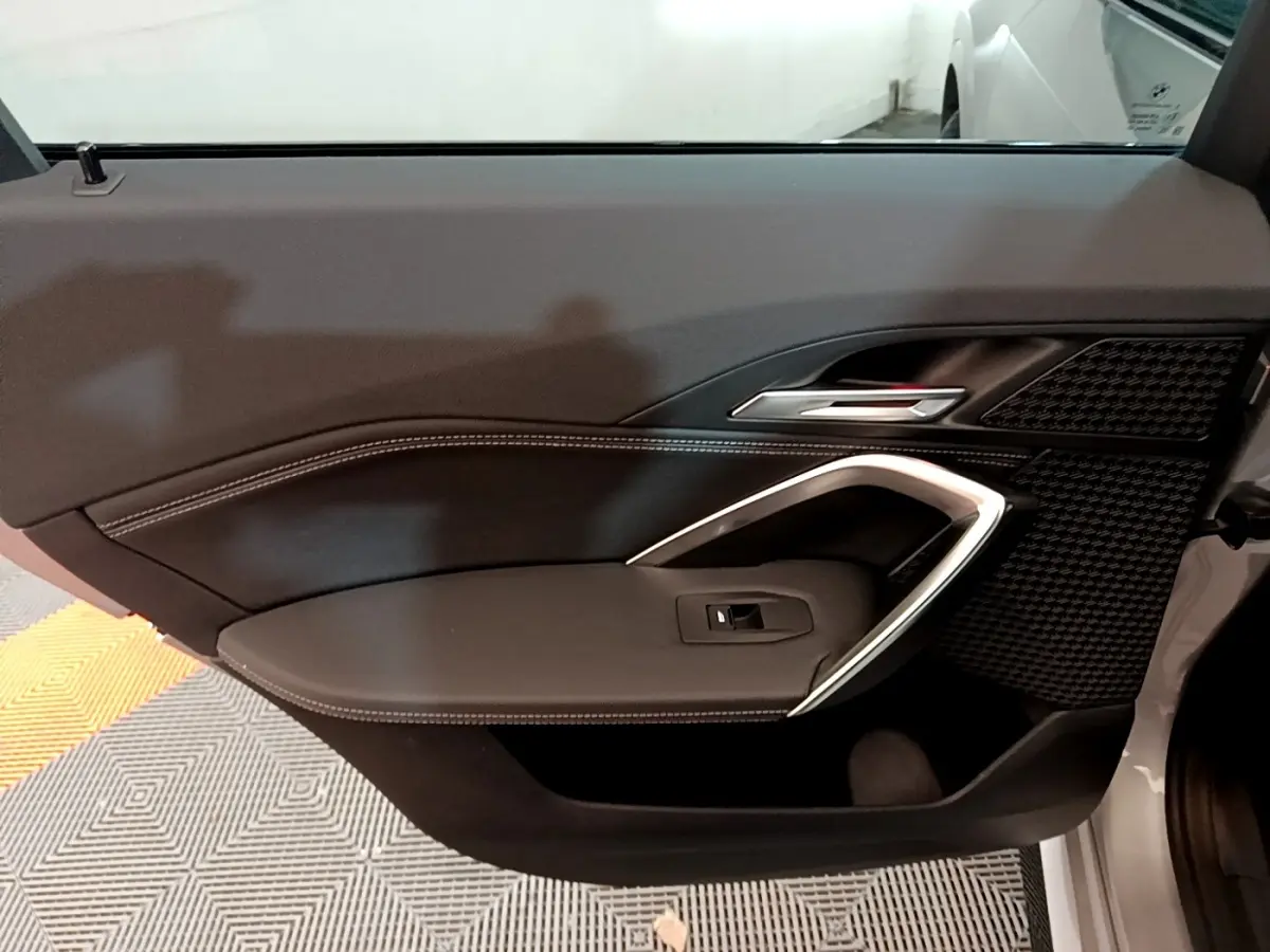 Gros plan sur la porte intérieure côté droit de la BMW X1 gris clair, avec poignée argentée et surpiqûres blanches.