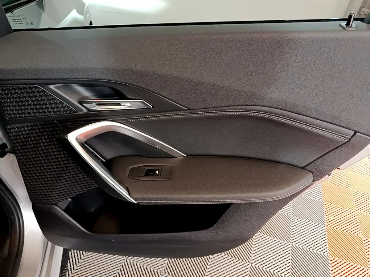Vue intérieure du panneau de porte côté gauche en cuir noir avec surpiqûres blanches d’un BMW X1 gris clair 2023.