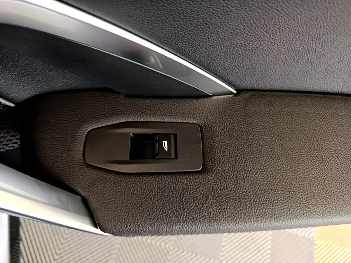 Détail du bouton de commande de la vitre sur la porte intérieure noire d’un BMW X1 xDrive23i M Sport gris clair.