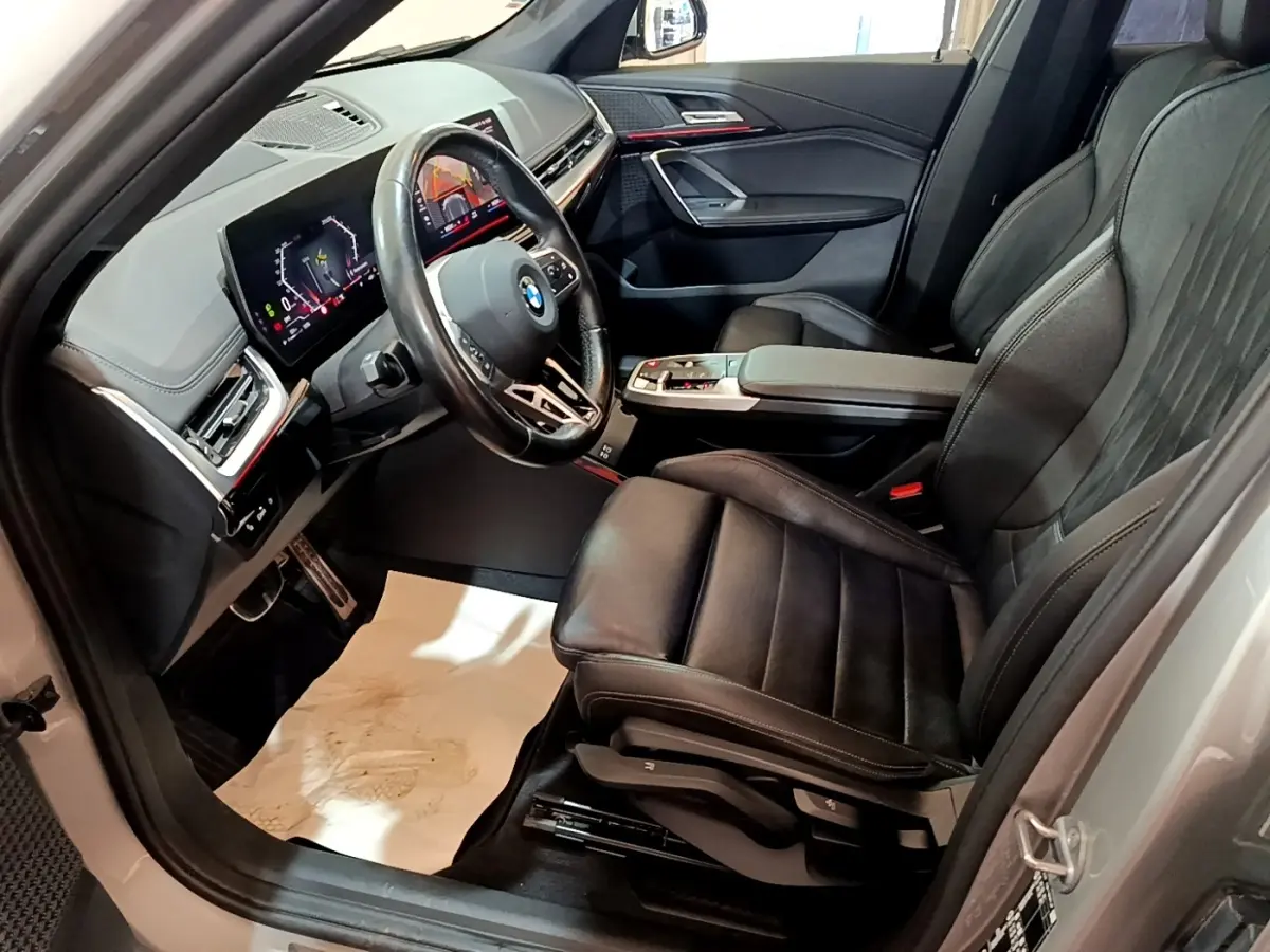 Vue intérieure côté conducteur du BMW X1 xDrive23i M Sport 2023, sièges cuir noirs et tableau de bord digital lumineux.