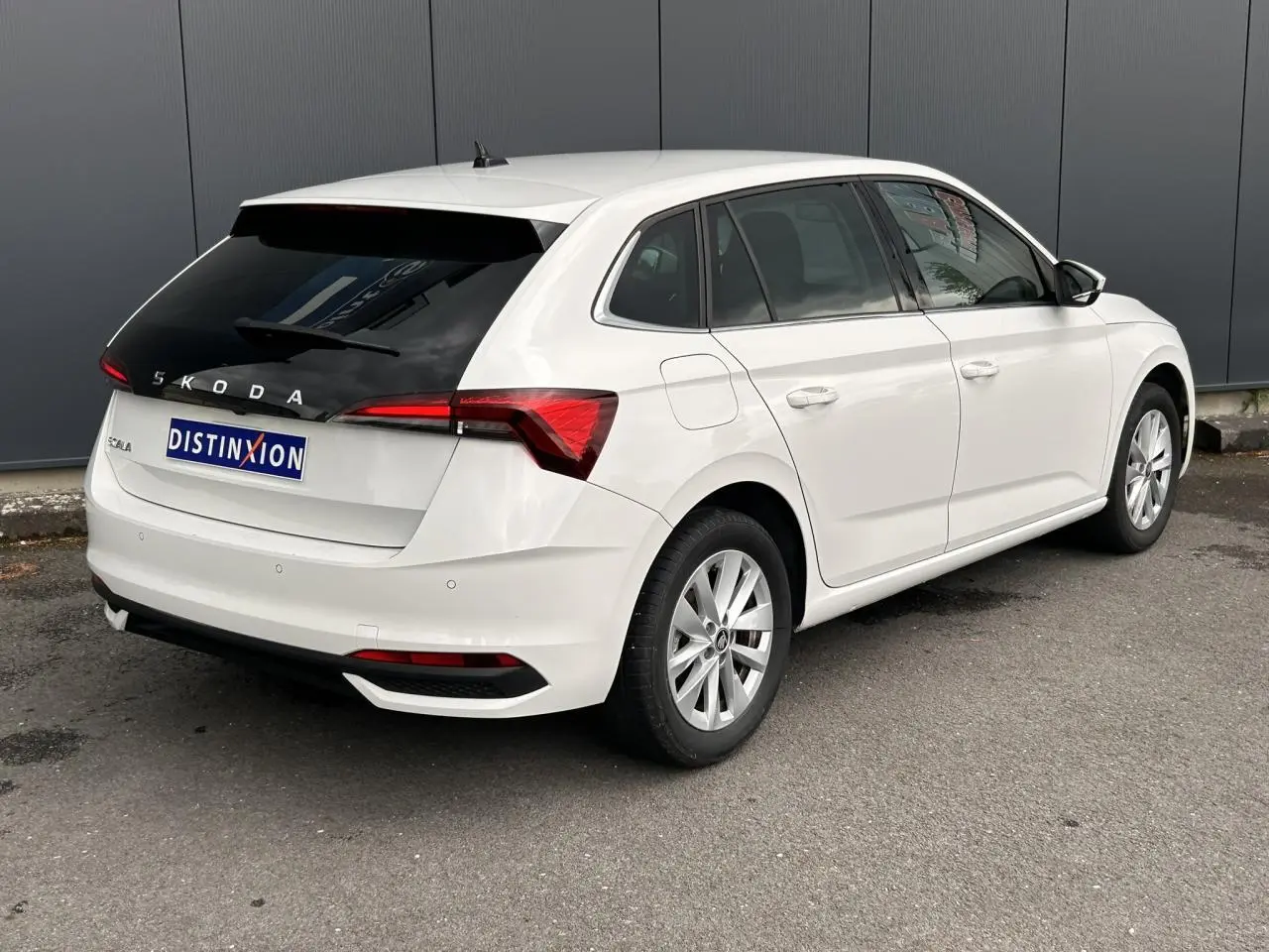 Vue 3/4 arrière droite d'une Skoda Scala blanche Candy avec lunette arrière surteintée et jantes alliage 16 pouces.
