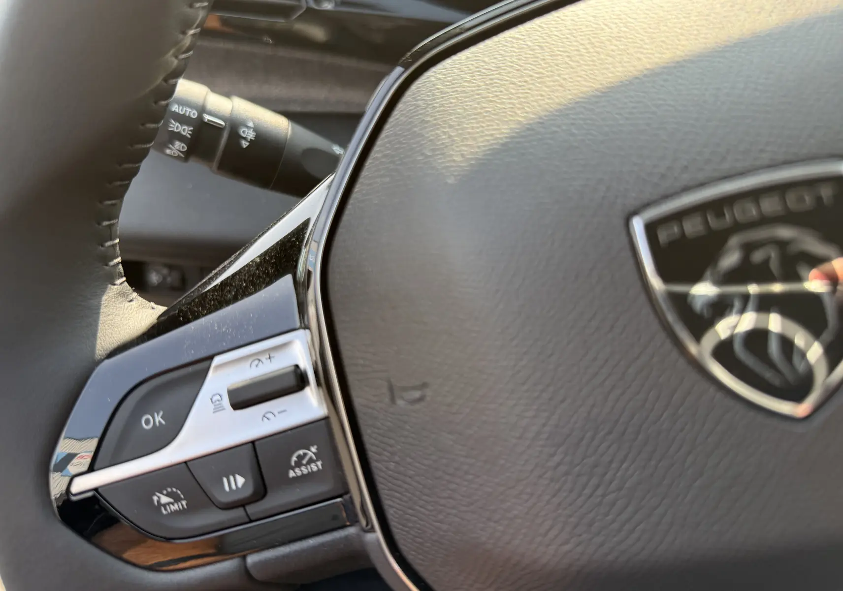 Gros plan sur le volant en cuir gris de la Peugeot 308 2025 avec commandes intégrées et logo lion central.