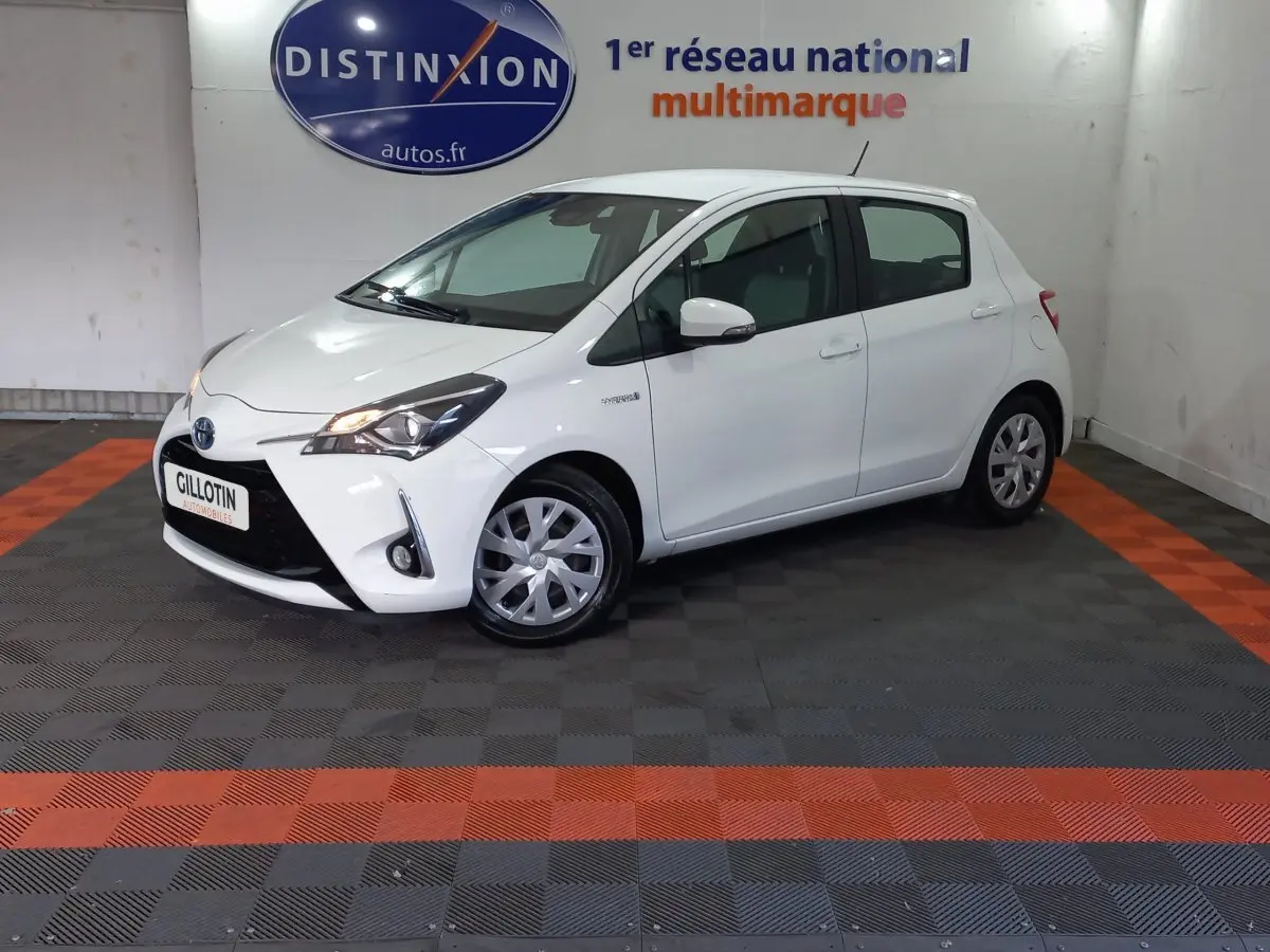 Toyota Yaris hybride blanche vue de profil avant droit dans un showroom avec logo Distinxion en arrière-plan.