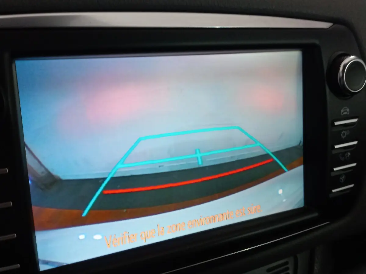 Vue de la caméra de recul de la Toyota Yaris blanche, affichant les lignes de guidage sur l'écran tactile du tableau de bord.