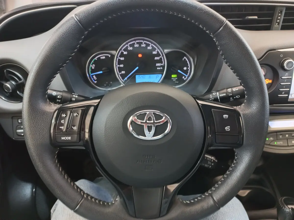 Vue rapprochée du volant cuir noir de la Toyota Yaris 2019 avec commandes multifonctions et tableau de bord lumineux.