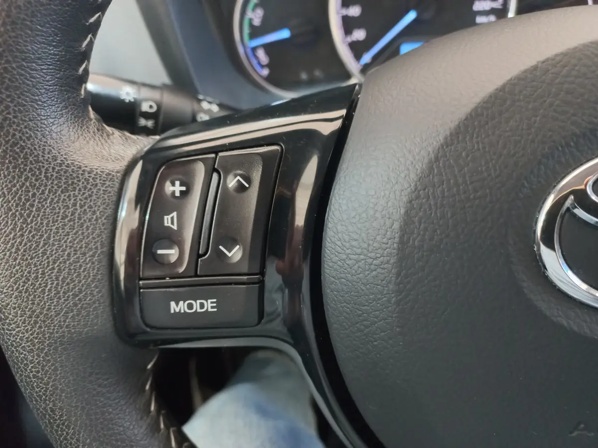 Gros plan sur les commandes gauche du volant en cuir noir de la Toyota Yaris hybride 2019, avec logo Toyota visible.