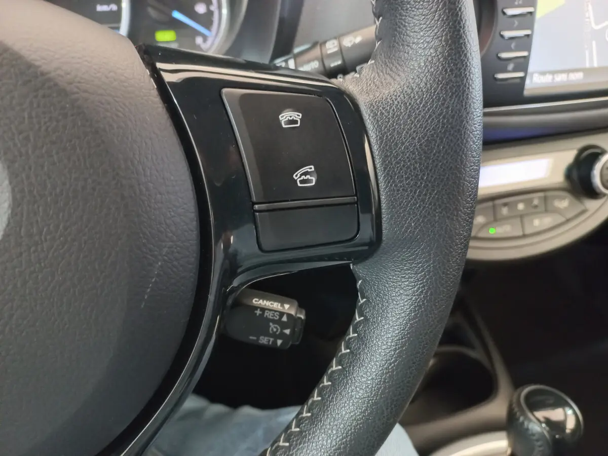Gros plan sur la partie droite du volant noir en cuir de la Toyota Yaris hybride, avec commandes téléphoniques et régulateur de vitesse.