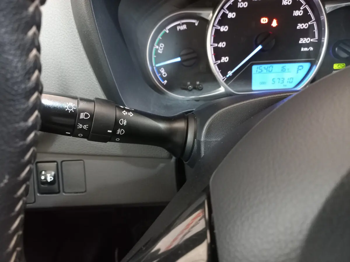 Gros plan sur le tableau de bord et la manette des phares de la Toyota Yaris hybride blanche, affichage digital visible.