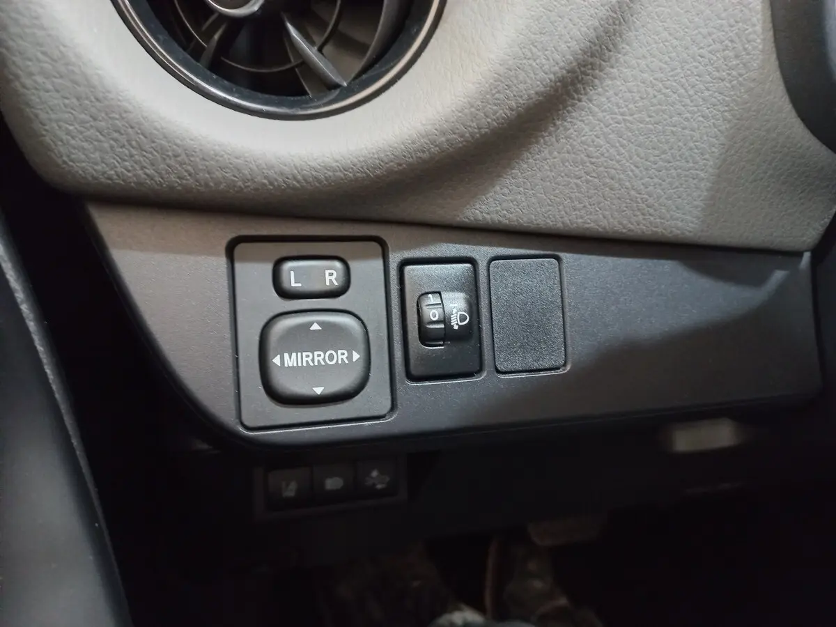 Gros plan sur les commandes de réglage des rétroviseurs et des phares dans une Toyota Yaris blanche 2019.
