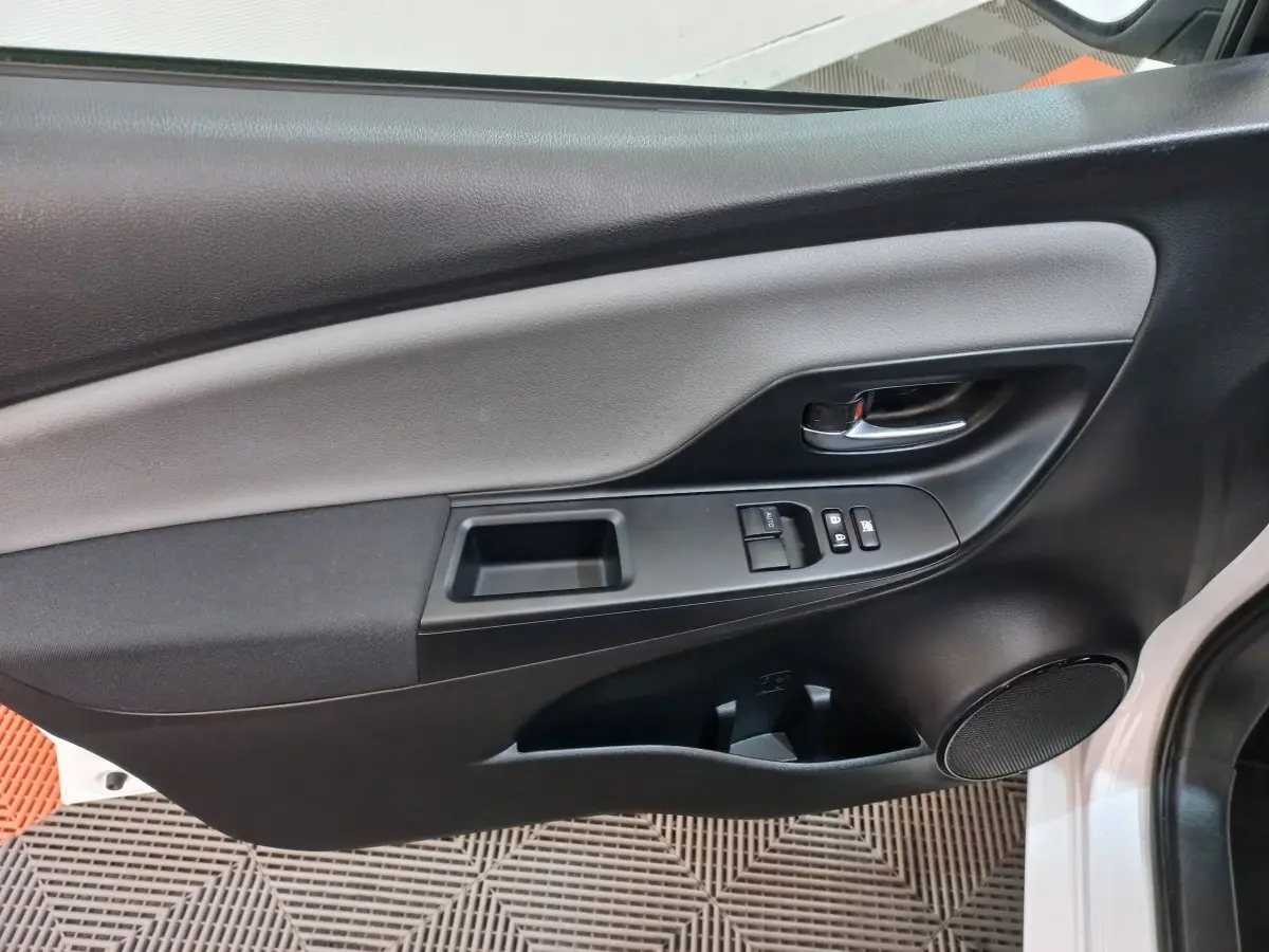 Panneau intérieur de porte côté gauche noir et gris de Toyota Yaris blanche, avec commandes de vitres et poignée chrome.