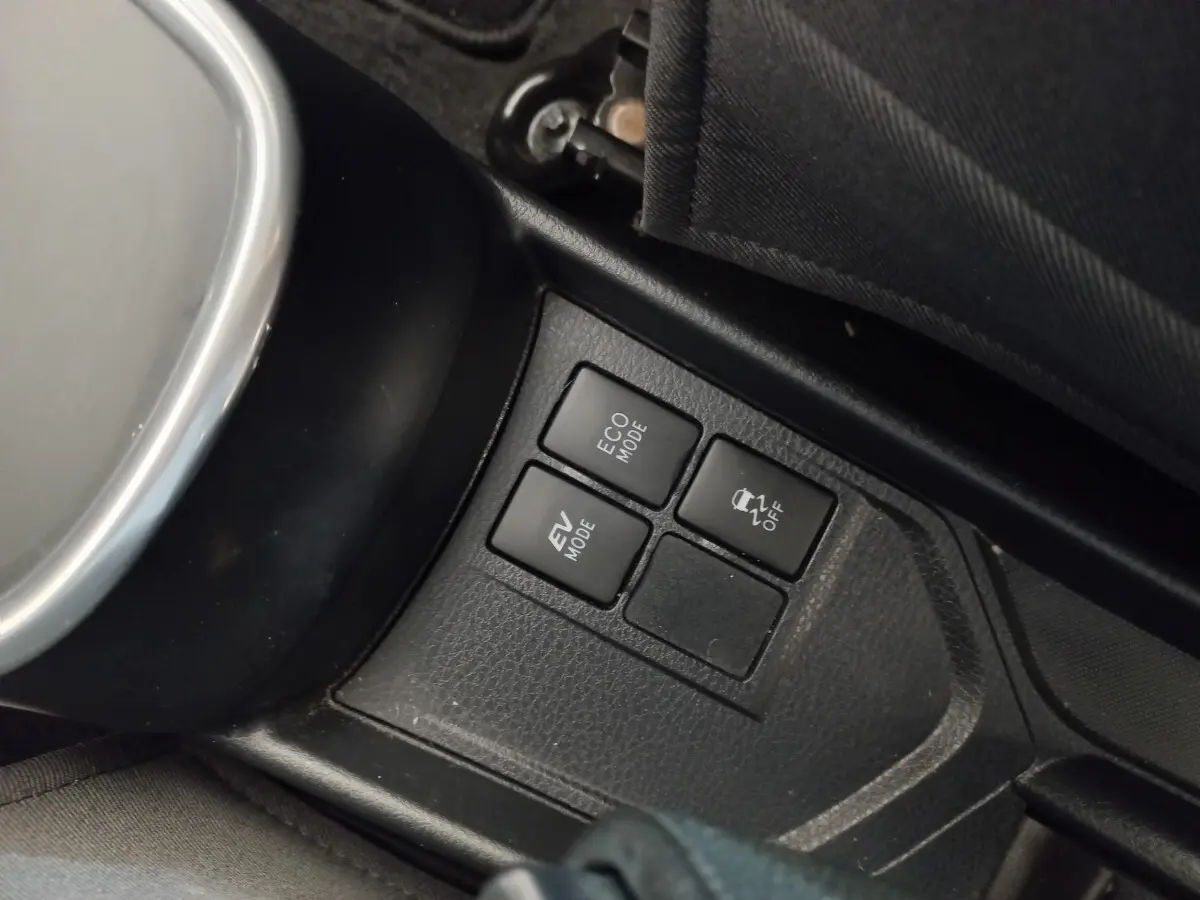 Gros plan sur les boutons de modes de conduite et contrôle de stabilité dans l'habitacle noir d'une Toyota Yaris hybride blanche.