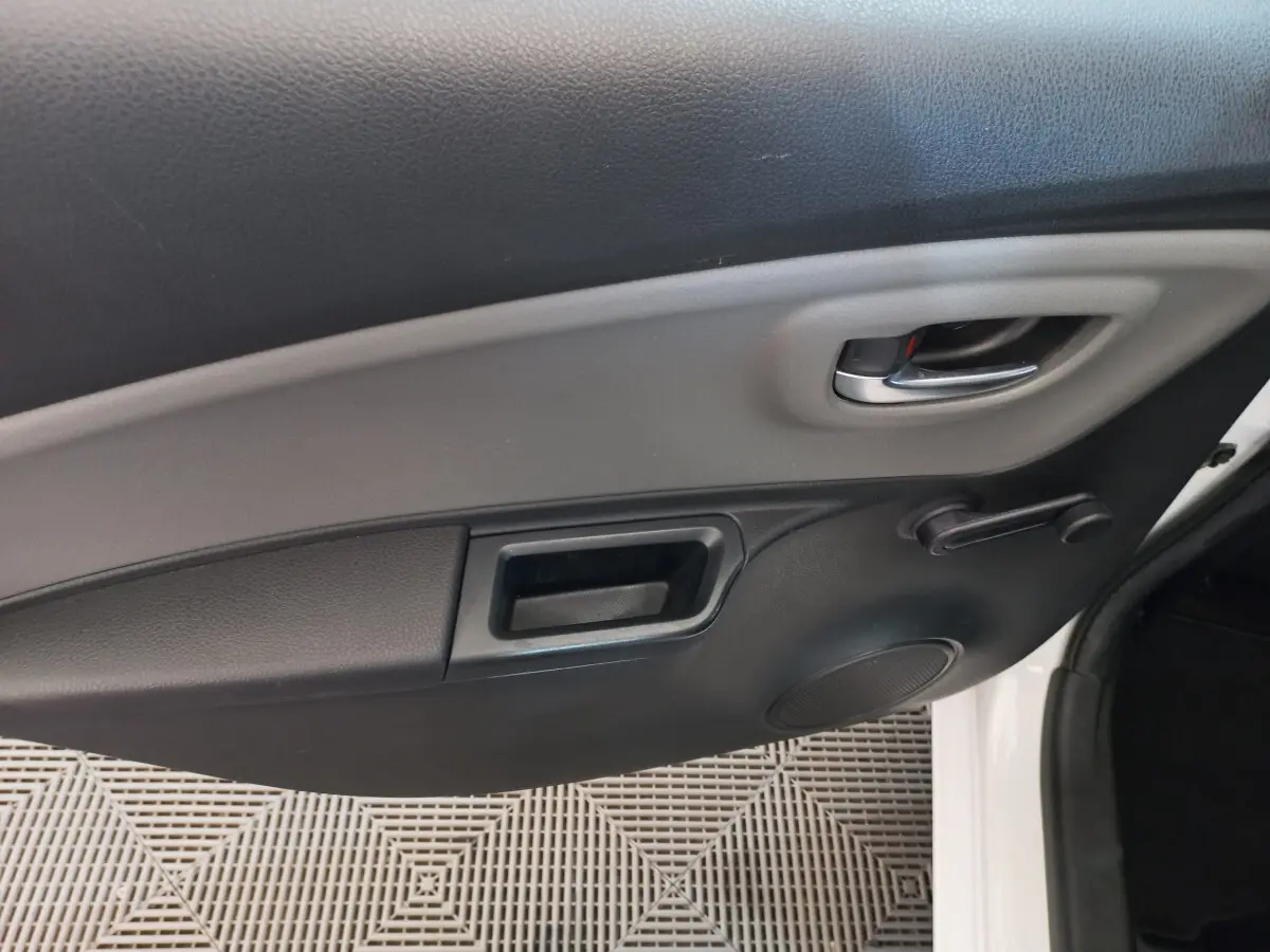 Poignée intérieure et manivelle de vitre côté droit de la porte d'une Toyota Yaris blanche, vue rapprochée.