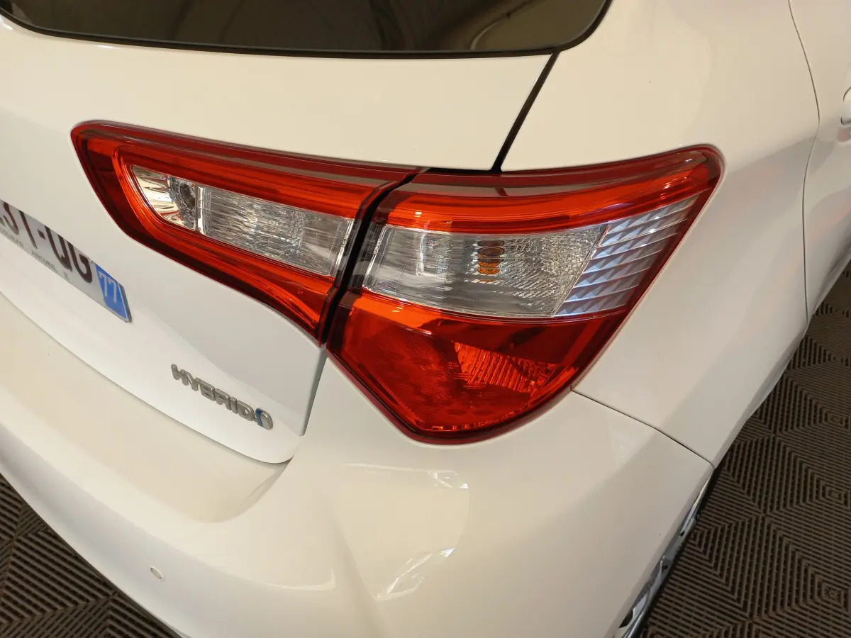 Gros plan sur le feu arrière droit d'une Toyota Yaris hybride blanche, avec logo Hybrid visible sur le coffre.
