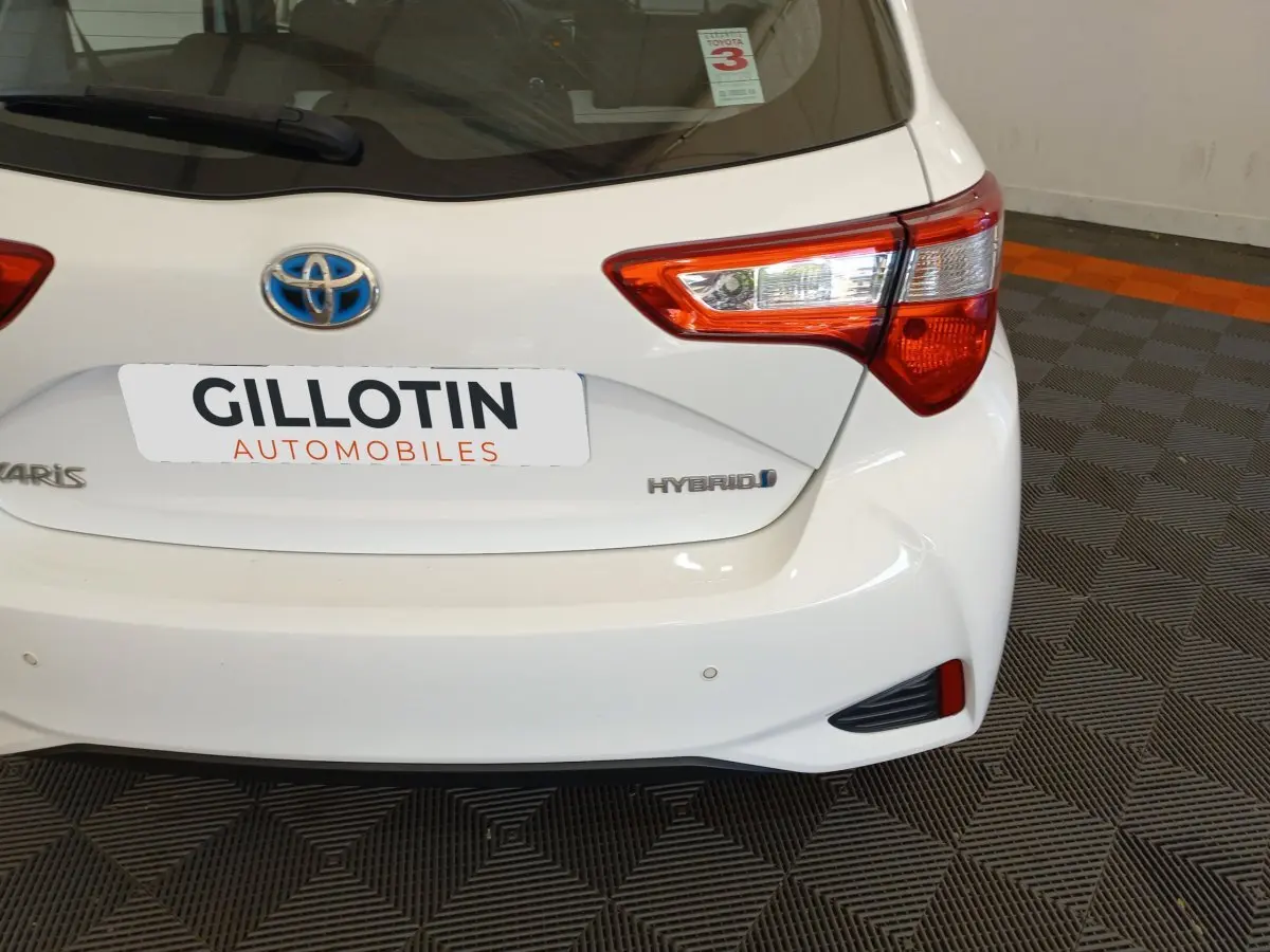 Vue arrière droite d'une Toyota Yaris blanche hybride 2019 avec feux arrière distinctifs et logo bleu Toyota.