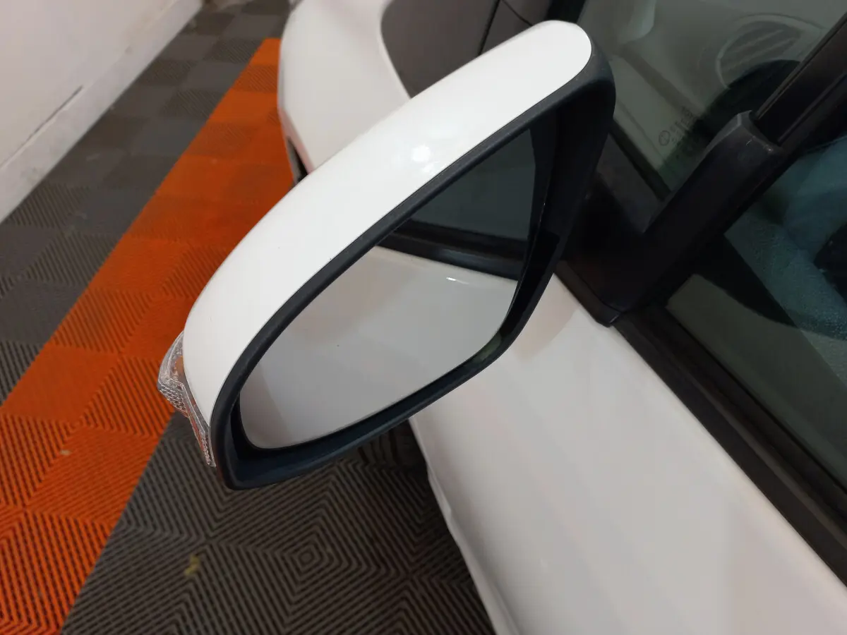 Rétroviseur côté gauche blanc de la Toyota Yaris 2019 hybride, avec clignotant intégré visible sur fond de sol orange et gris.