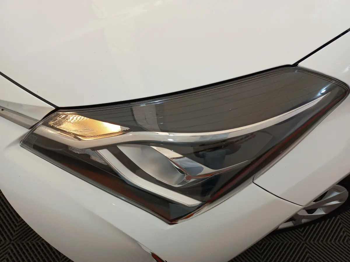Gros plan sur le phare avant gauche allumé d'une Toyota Yaris blanche 2019 version hybride France Business.