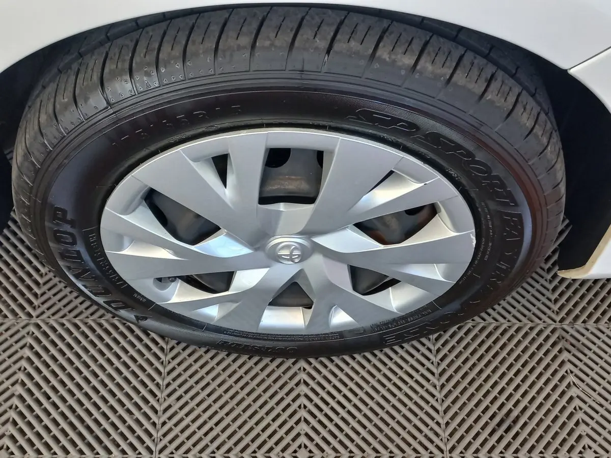 Gros plan sur la roue avant droite d'une Toyota Yaris blanche, avec jante argentée et pneu Dunlop visible.