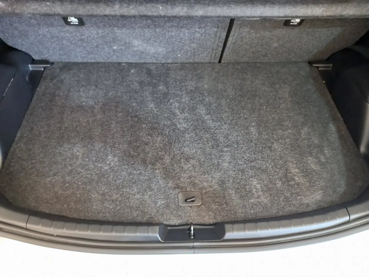 Coffre ouvert d'une Toyota Yaris blanche, vue de dessus montrant la surface de chargement avec tapis gris.