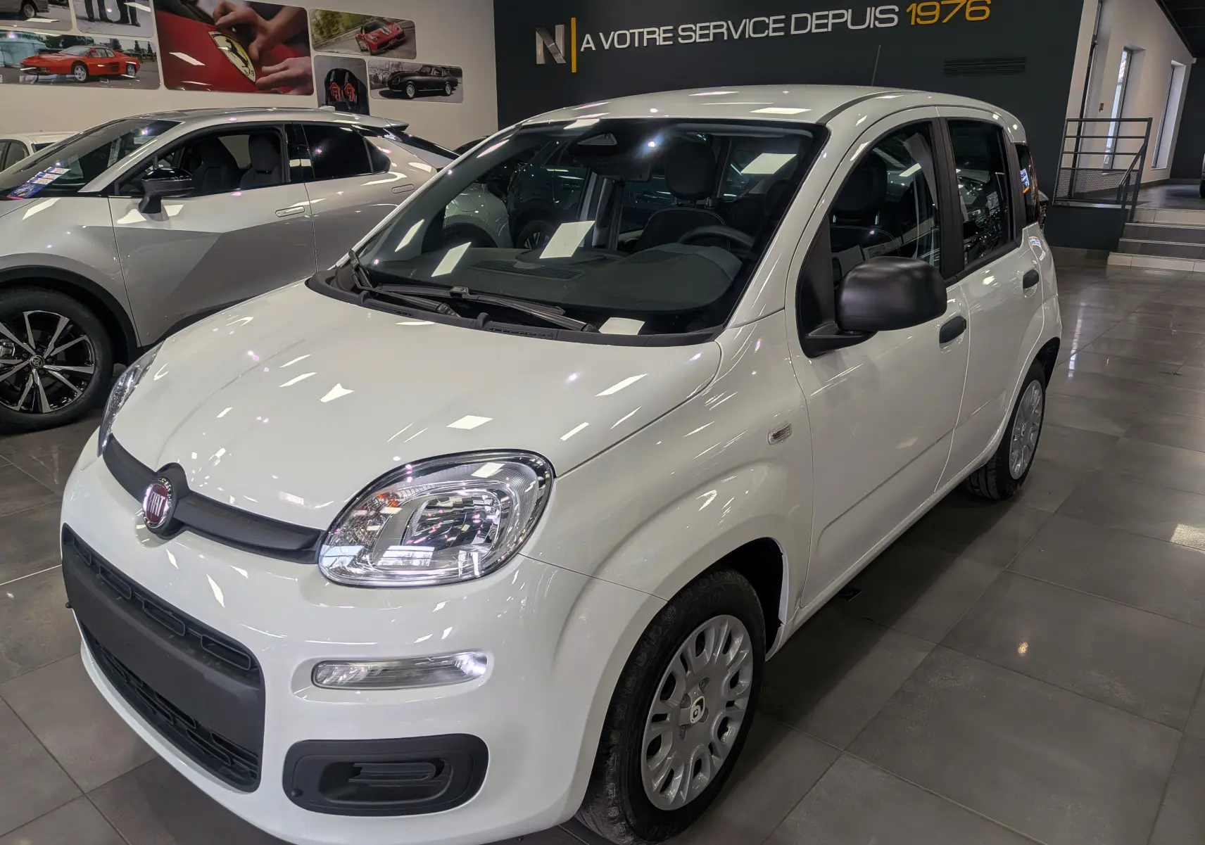Vue 3/4 avant droite d'une Fiat Panda 1.0 Hybrid City blanche Gelato en showroom avec rétroviseurs noirs.