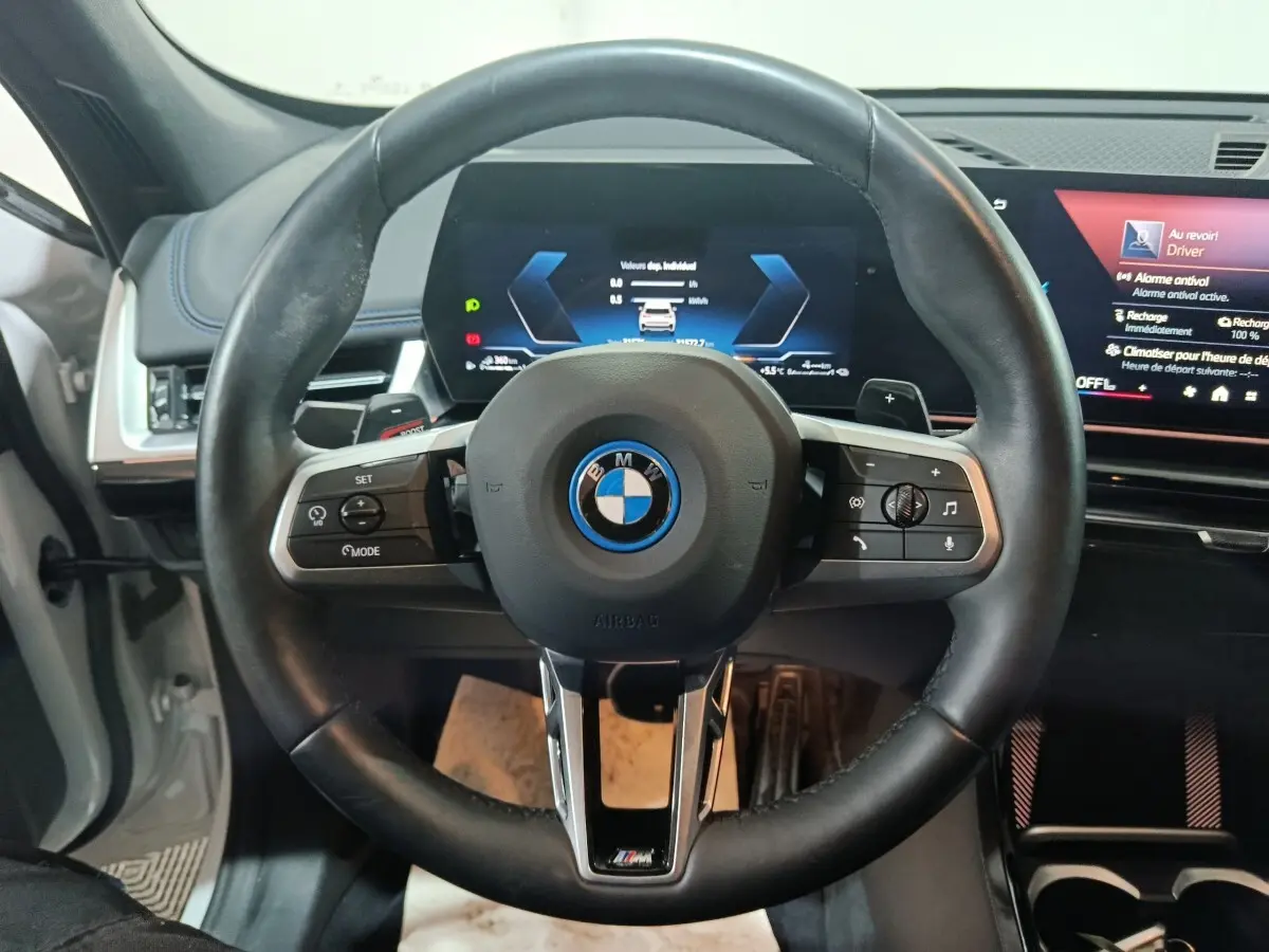 Vue centrée sur le volant cuir noir BMW X1 xDrive25e 2024 avec tableau de bord digital et écran tactile.