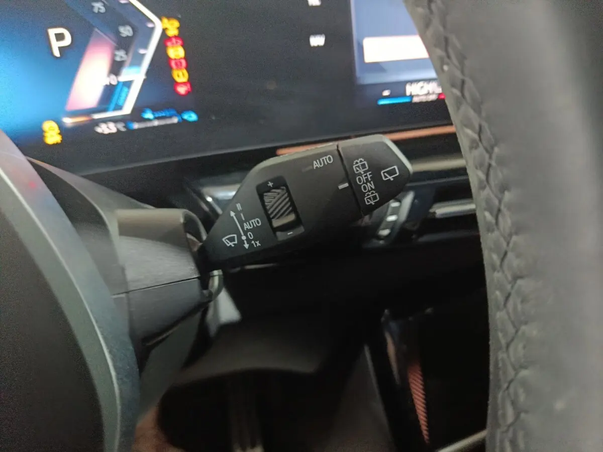 Gros plan sur la manette de commande des essuie-glaces et tableau de bord numérique d'une BMW X1 blanche 2024.