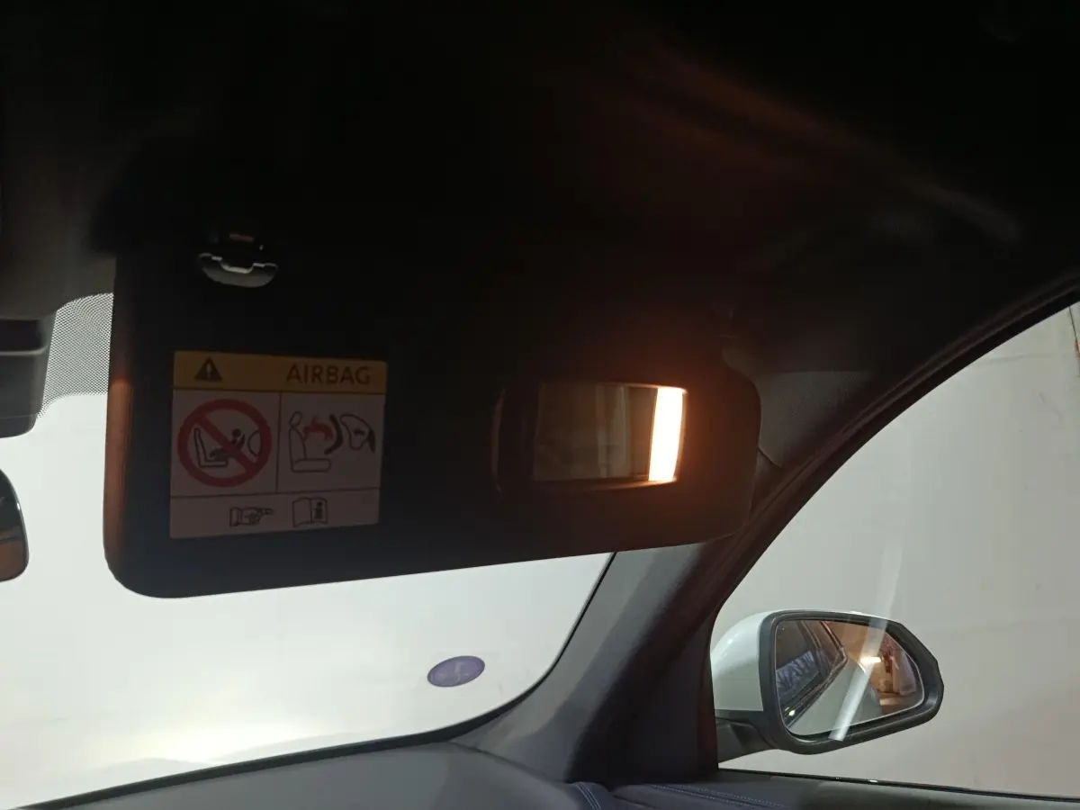 Vue intérieure côté conducteur du BMW X1 blanc 2024, avec pare-soleil baissé et miroir éclairé, rétroviseur extérieur visible.