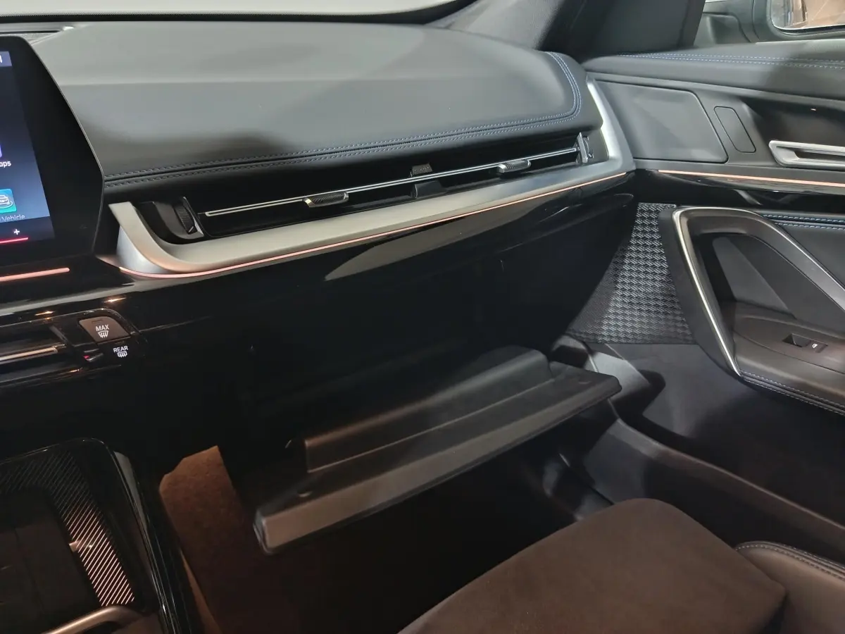 Intérieur de la BMW X1 xDrive25e 2024, vue côté passager sur la boîte à gants ouverte et tableau de bord noir.