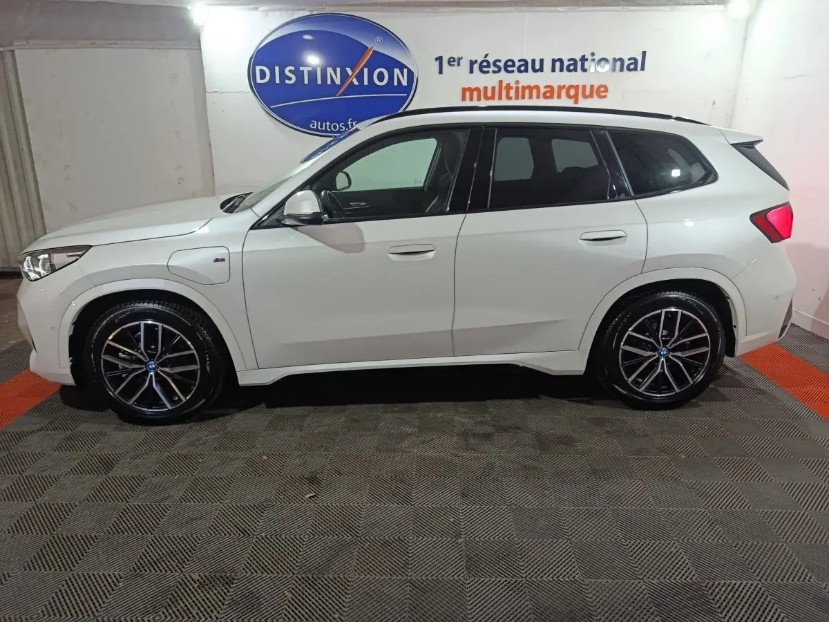 Vue de profil côté gauche d’un BMW X1 blanc xDrive25e M Sport avec jantes noires et logo M sur aile avant.