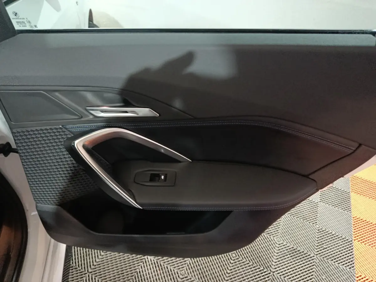 Détail de la porte intérieure côté gauche noire avec surpiqûres bleues et poignée argentée d’un BMW X1 blanc 2024.