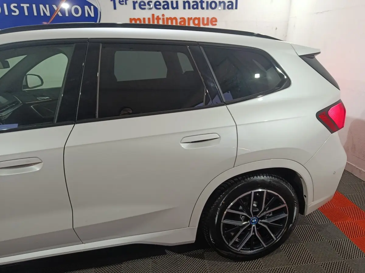 Vue latérale droite sur l'arrière d'un BMW X1 blanc avec jantes alliage et feux arrière LED visibles.