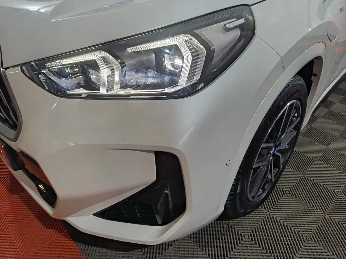 Gros plan sur l'avant droit blanc du BMW X1 xDrive25e M Sport 2024, mettant en valeur le phare LED et la jante noire.